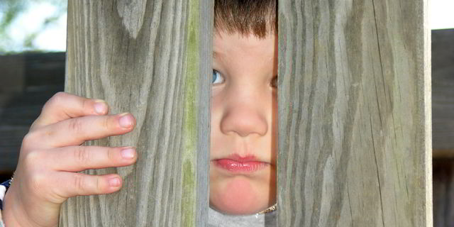 Sad boy peeking through wooden fence